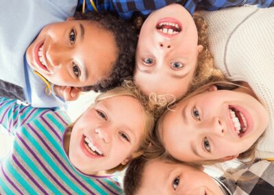 Five children stand in a circle, smiling up at the camera in bright, casual clothing. Their joyful expressions show the impact donations help hungry children through Stillwater OK nonprofit charity to end childhood hunger. -Kickin' Childhood Hunger