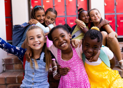 A group of smiling children sit on steps in front of red lockers, hugging and posing happily for the camera—thanks to donations that help hungry children, they enjoy each other's company at school. -Kickin' Childhood Hunger